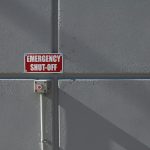 Czerwony przycisk awaryjnego wyłączenia z tabliczką „Emergency Shut-Off” zamontowany na betonowej ścianie.