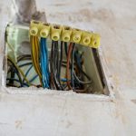 Kolorowe przewody elektryczne połączone w kostce instalacyjnej wewnątrz puszki w ścianie podczas prac elektrycznych.